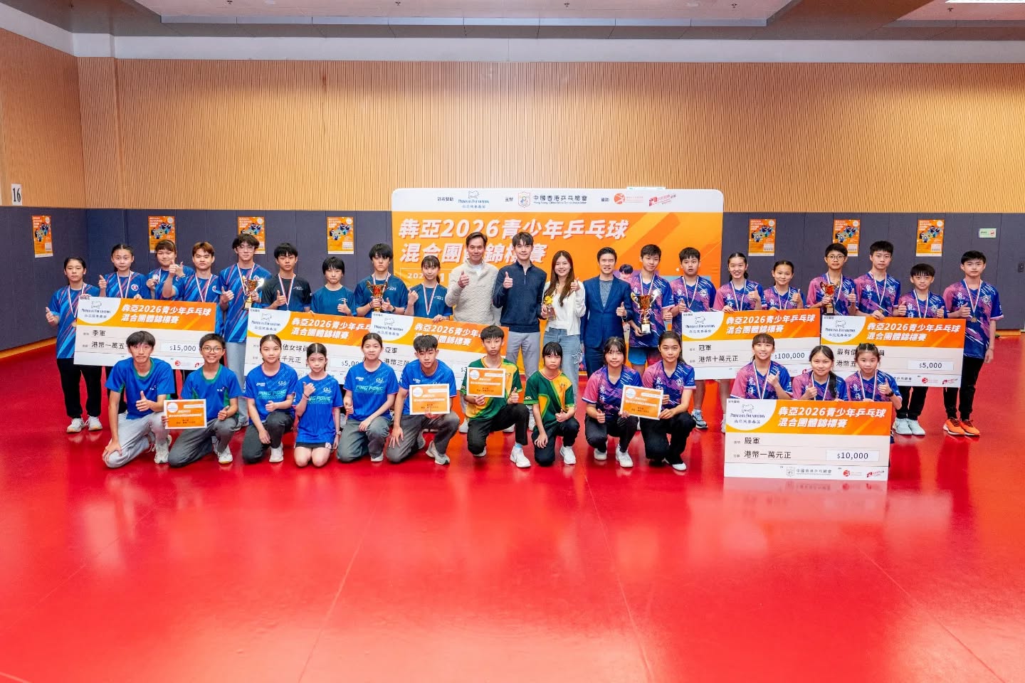Group photograph of youth table tennis players in team uniforms with trophies and prize cheques in front of the Primasia 2026 tournament banner.